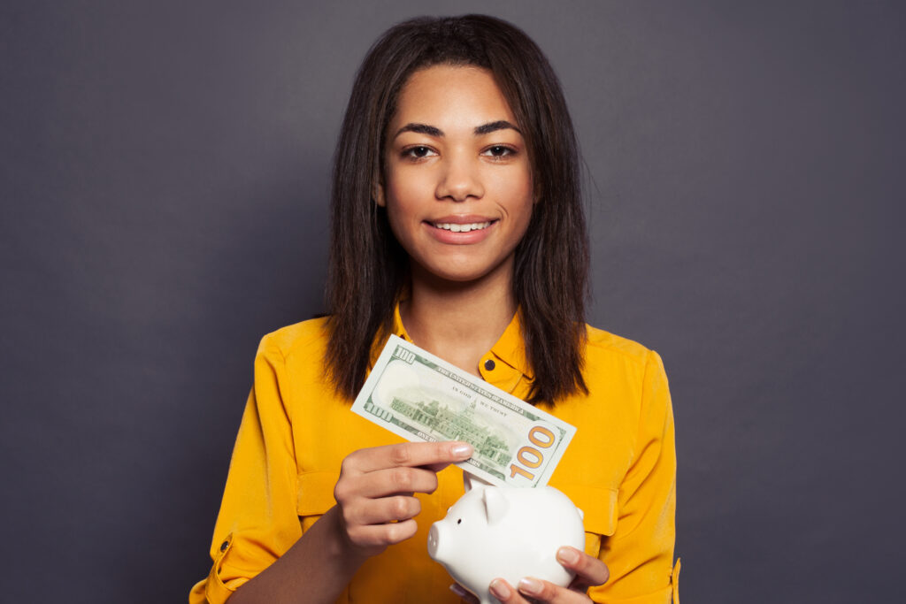 22 03 07 a person putting a 100 dollar bill into a piggy bank gettyimages 1203959263